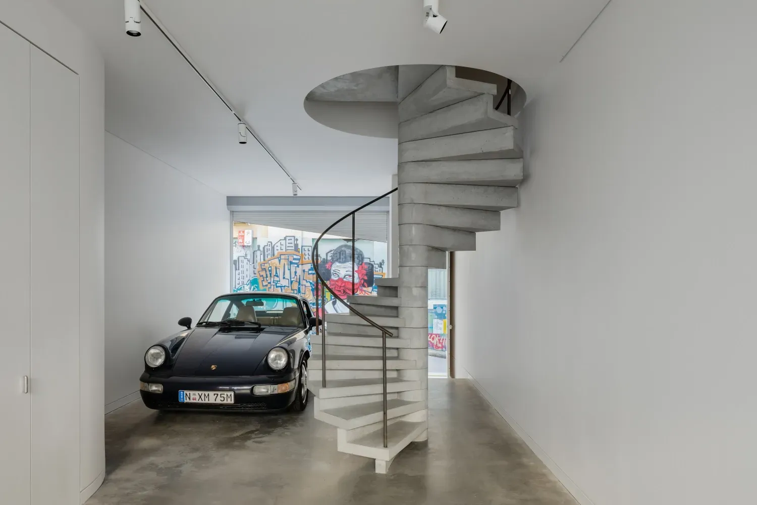 A car is parked in a garage next to a spiral staircase.