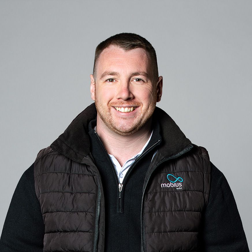 A man wearing a black vest and a black sweater is smiling for the camera.
