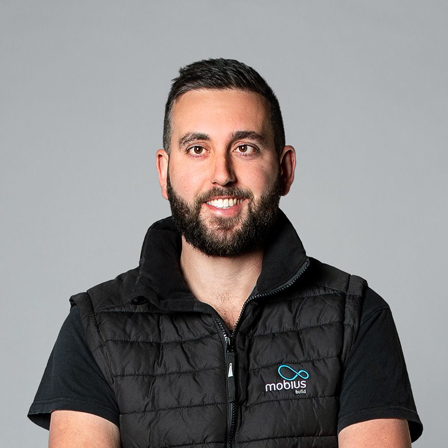 A man with a beard is wearing a black vest and smiling.