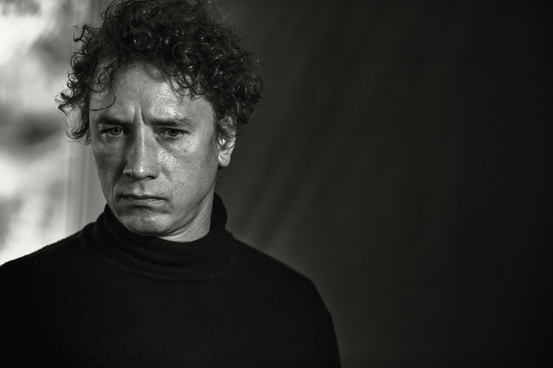 A black and white photo of a man with curly hair wearing a turtleneck.