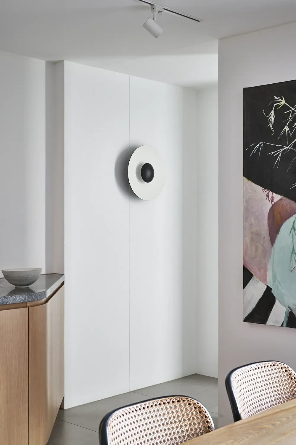 A dining room with a table and chairs and a painting on the wall.