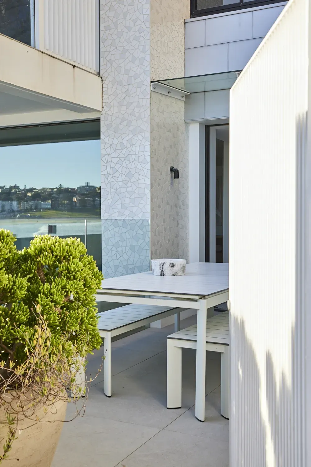 A white table and benches on a balcony with a potted plant in the foreground.