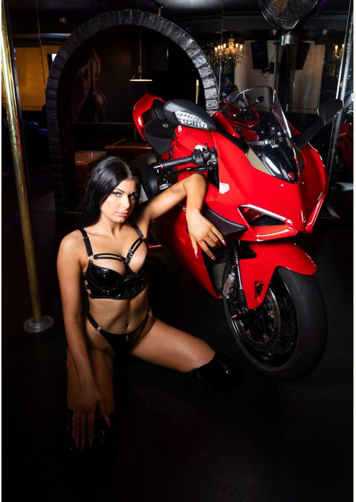 Woman in black leather near a red motorcycle, kneeling in a club setting. — Mens Gallery in Hobart, TAS
