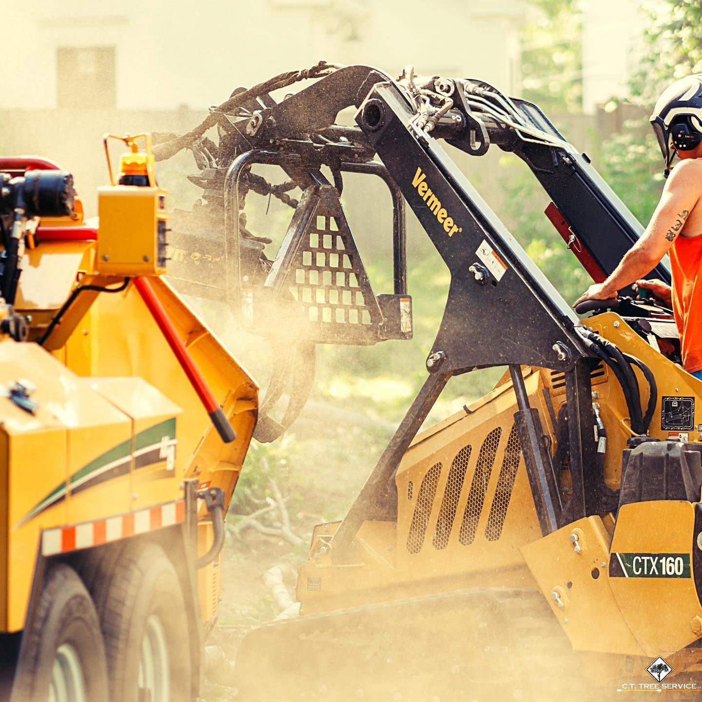 Yellow Vermeer CTX160 clearing brush, operator wearing helmet; yellow trailer nearby.