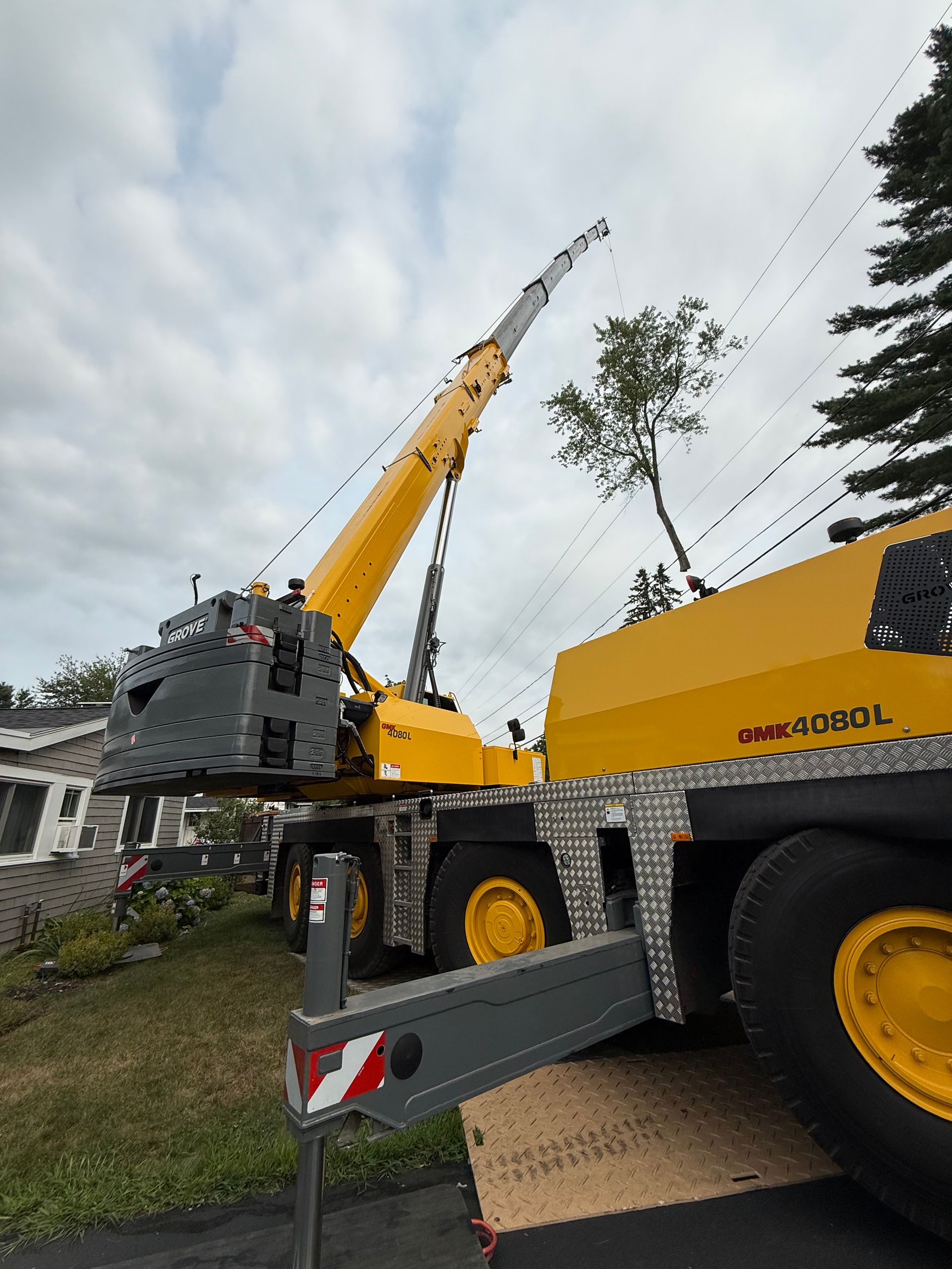 Yellow mobile crane near a house with an extended boom under a cloudy sky.