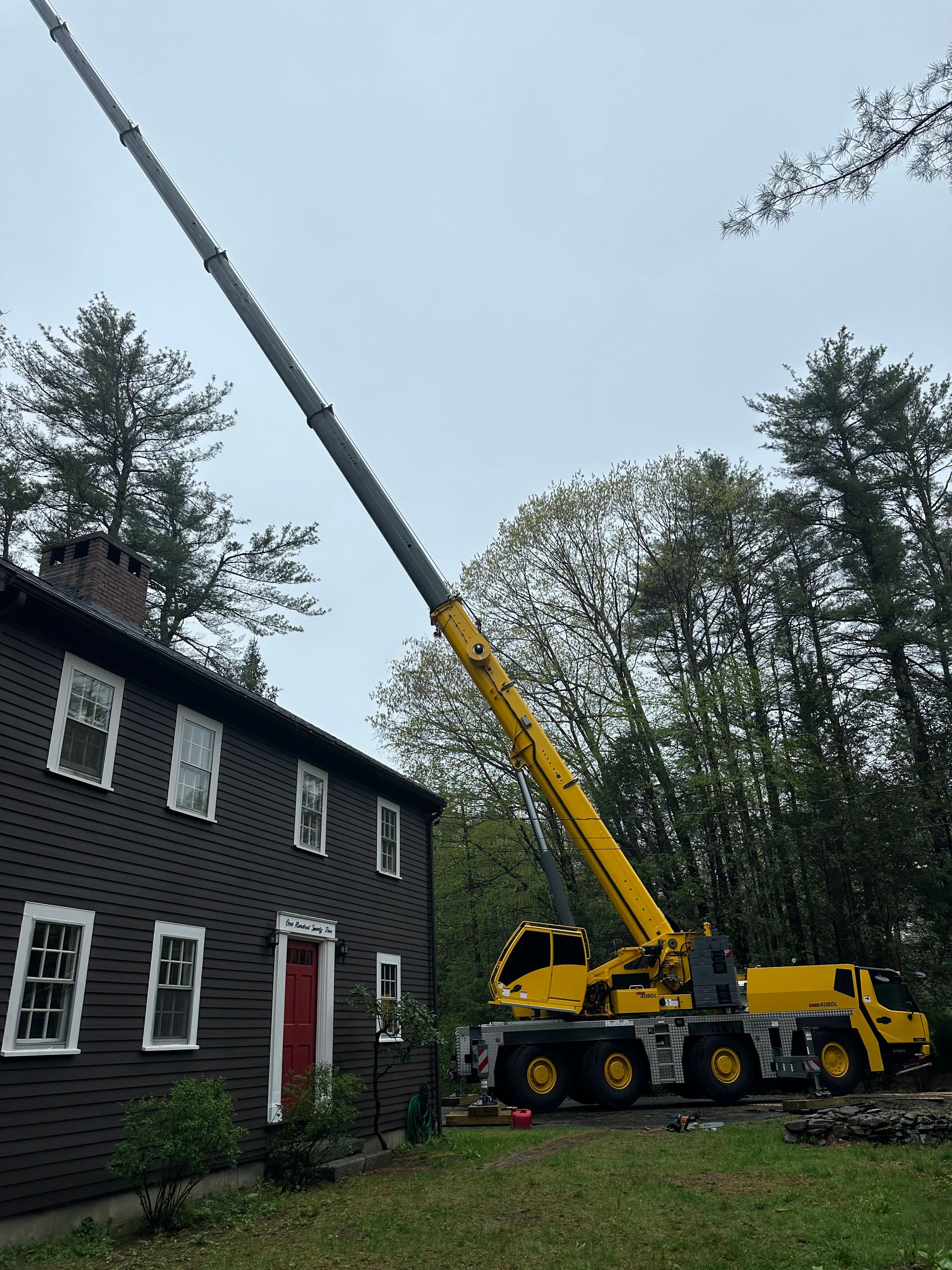 A yellow crane next to a dark house, trees in background, overcast sky.
