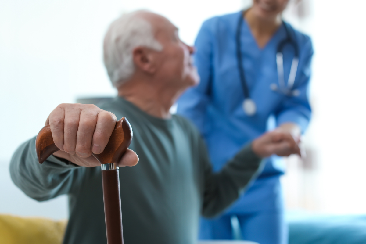 An elderly man with a cane is standing next to a nurse.
