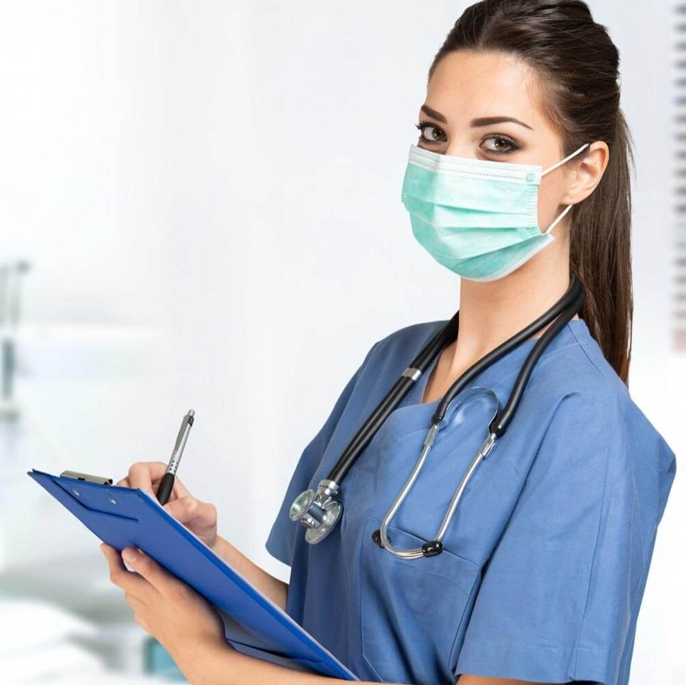 A nurse wearing a mask is writing on a clipboard