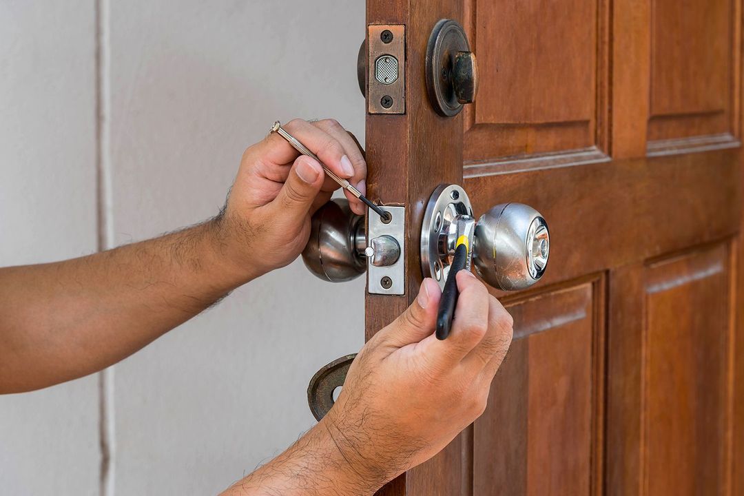 Hands installing a silver doorknob on a wooden door with a screwdriver