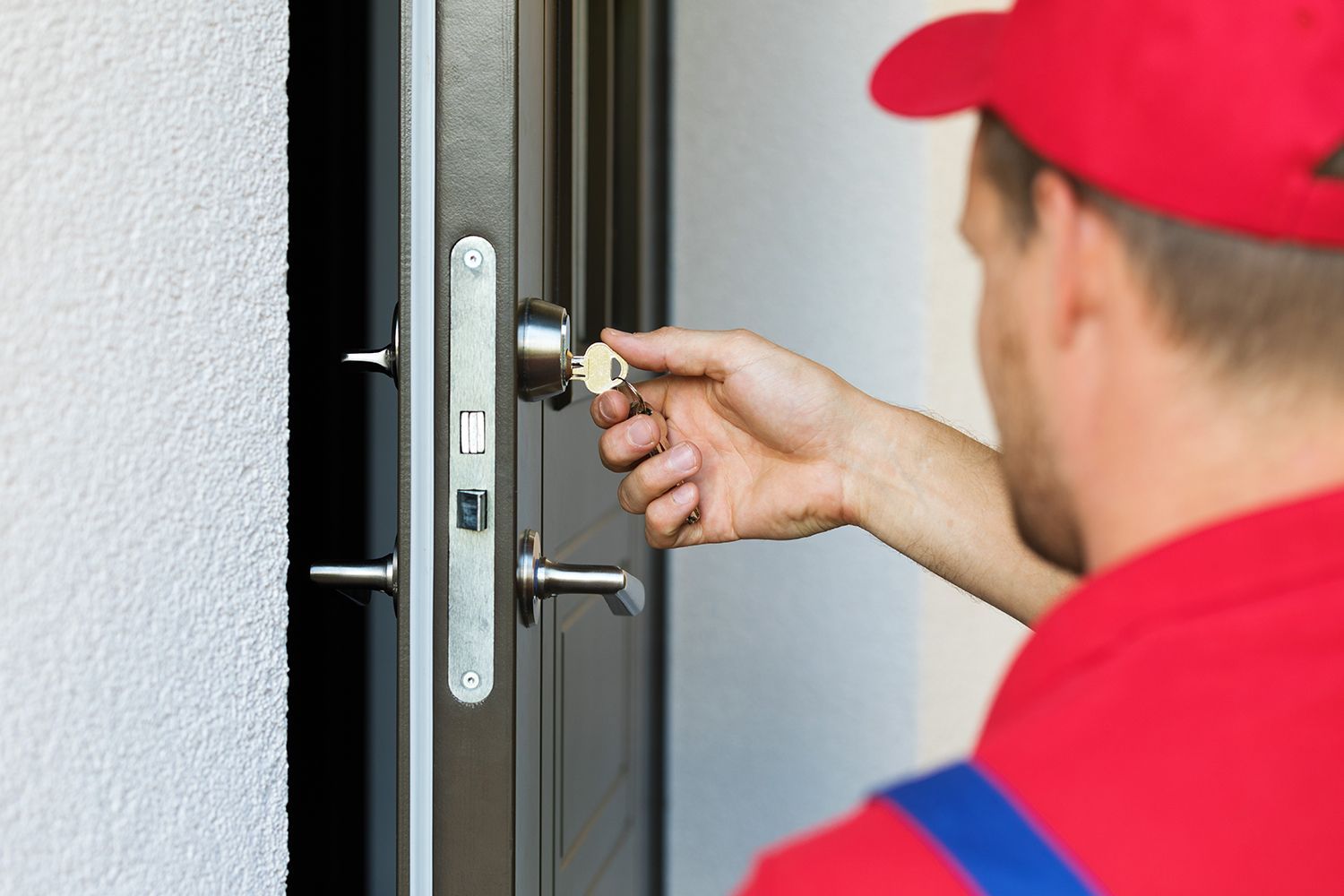 Person in red cap unlocking a gray door with a key
