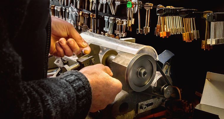 Hands using a key-cutting machine with rows of keys hanging in the background.