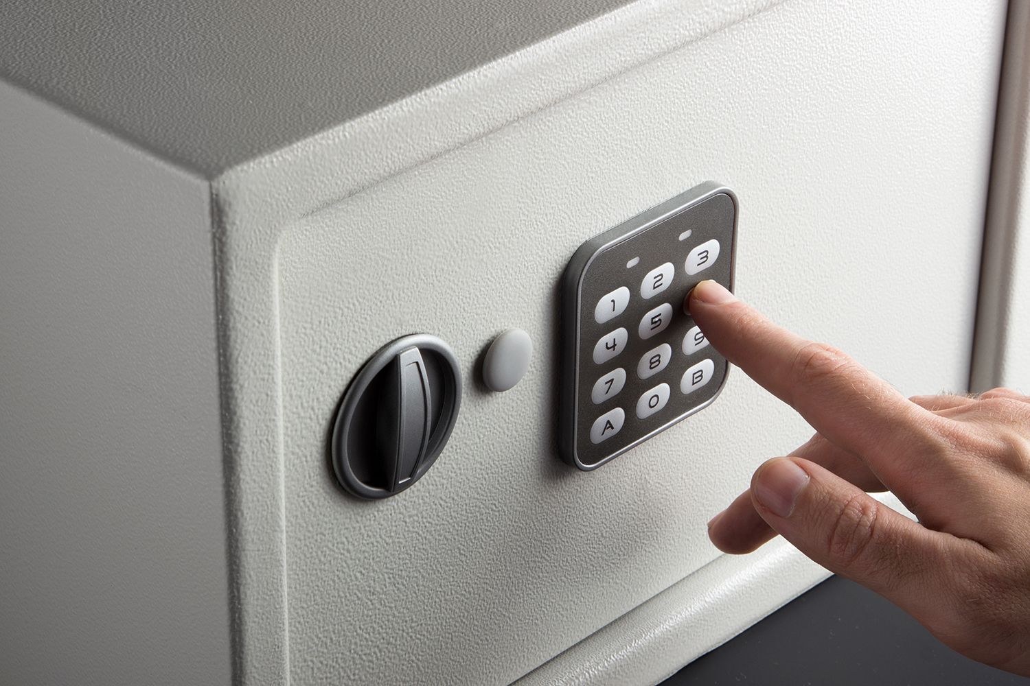 Hand pressing a keypad on a gray wall safe with a round lock