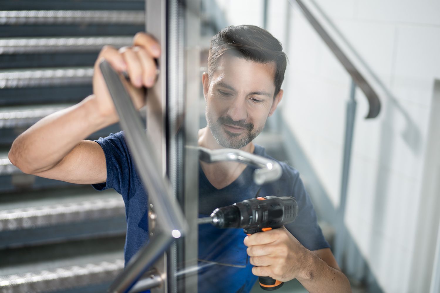 Man using a power drill to work on a stair railing indoors