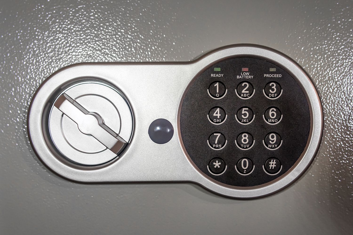 Close-up of a silver digital safe with a round keypad and keyhole on a gray surface
