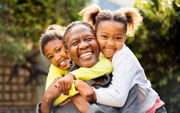 Woman smiling, embraced by two children outdoors.