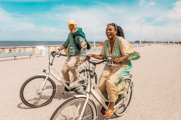 Couple riding bicycles along a seaside path; sunny day, smiles.
