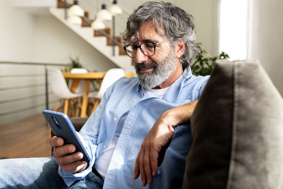 Man with glasses using a smartphone while sitting on a couch. Living room setting.
