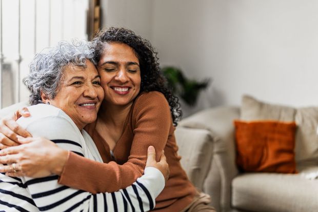 Woman embracing an older person, both smiling; seated on a sofa indoors.