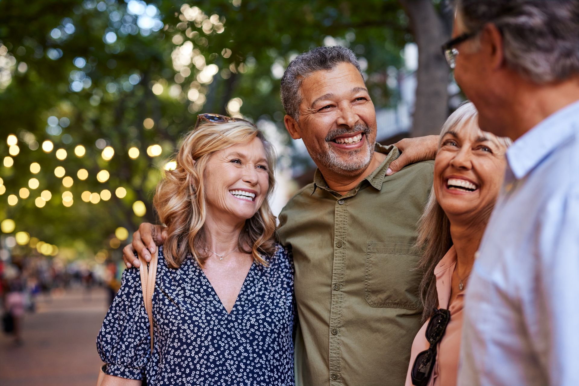 Four people smiling, conversing outdoors; warm lighting.