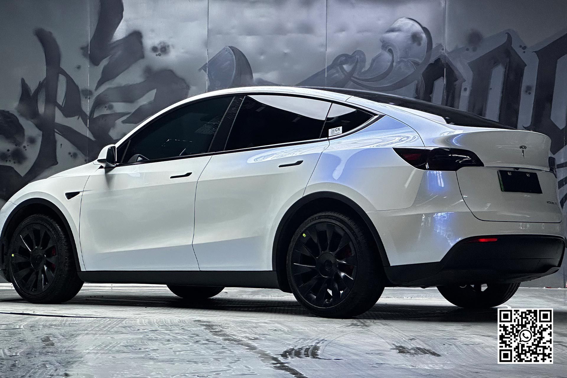 una tesla model y bianca è parcheggiata davanti a un muro di graffiti .