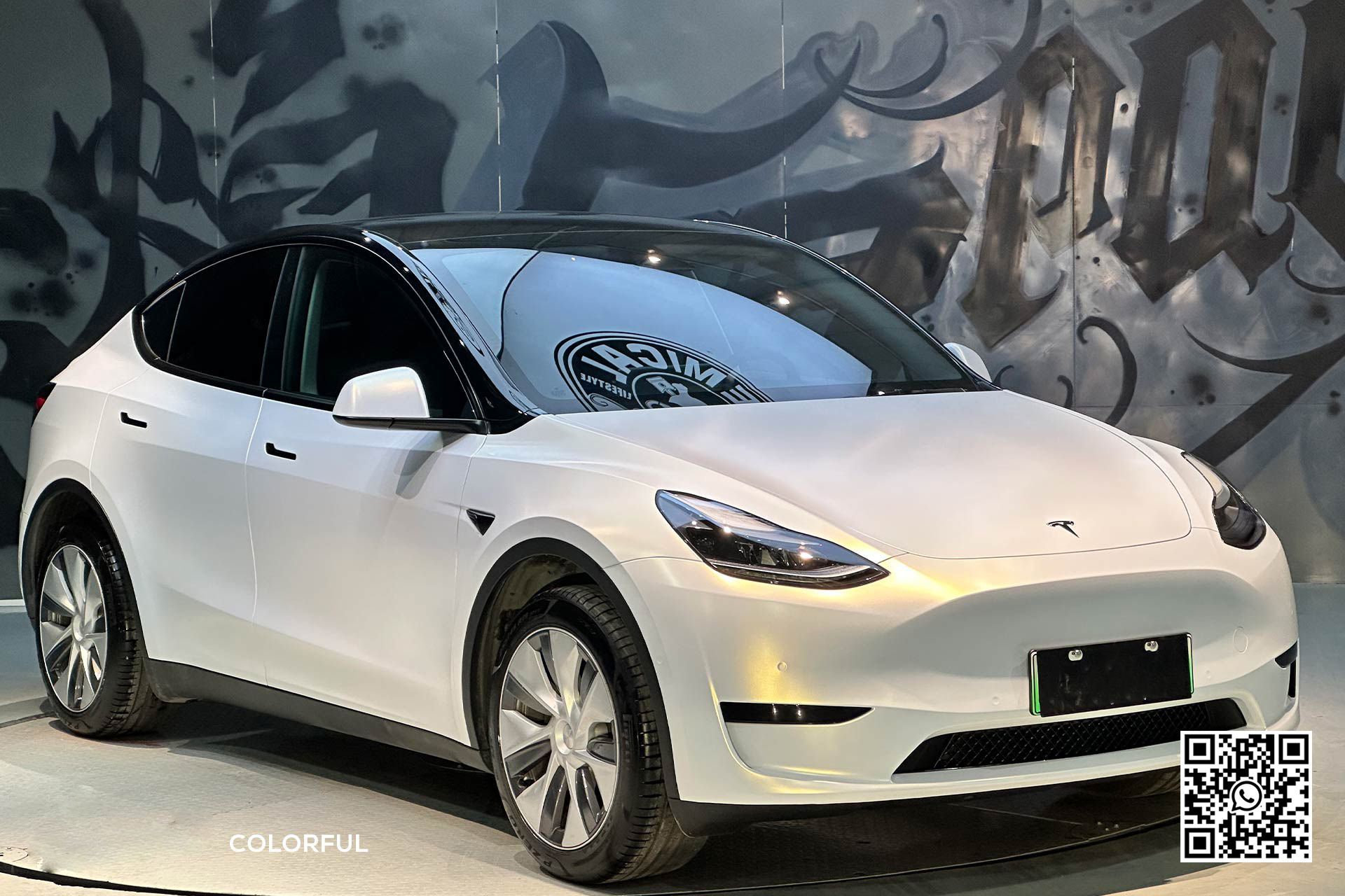 una tesla model y bianca è parcheggiata davanti a un muro di graffiti .