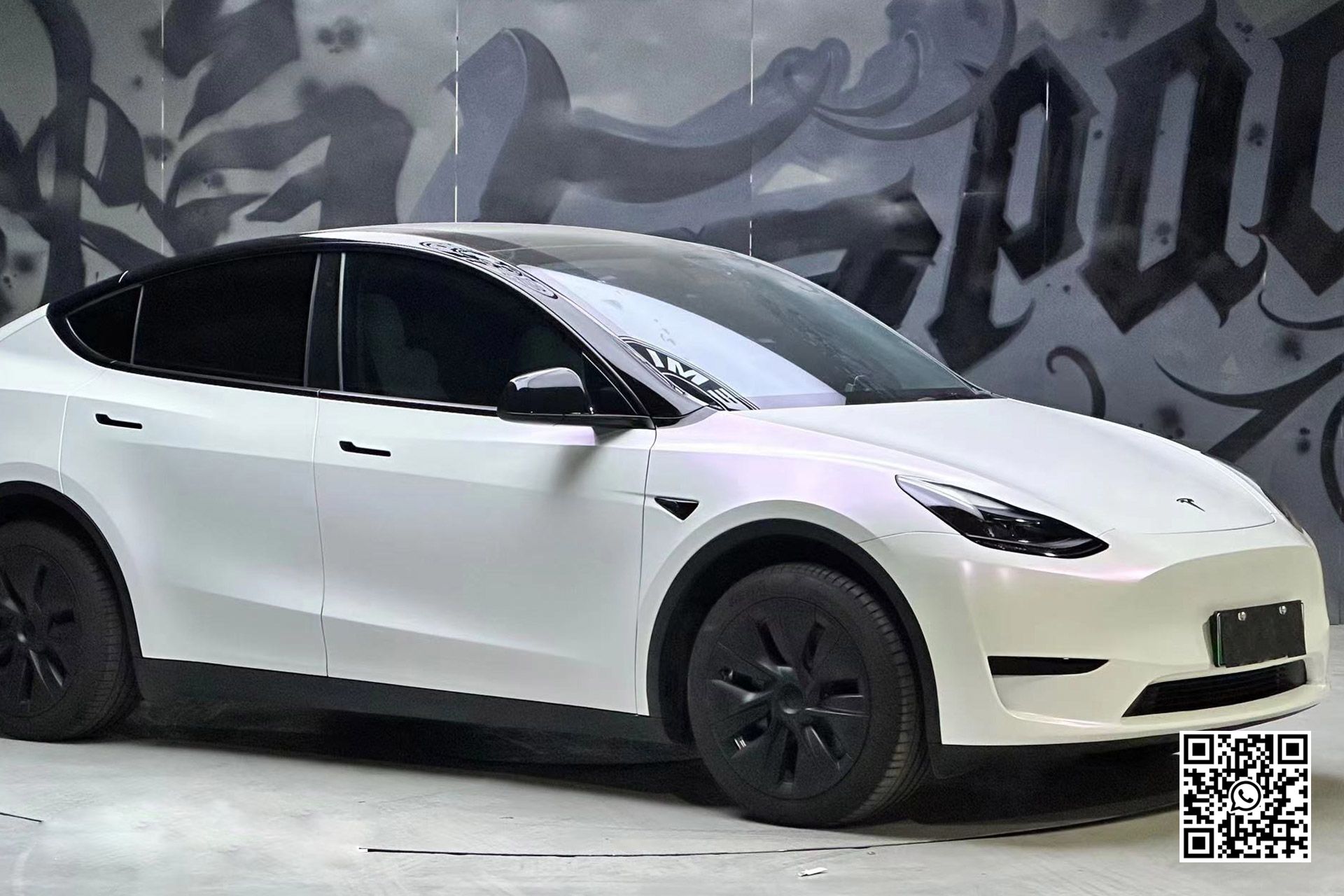 una tesla model y bianca è parcheggiata davanti a un muro di graffiti .