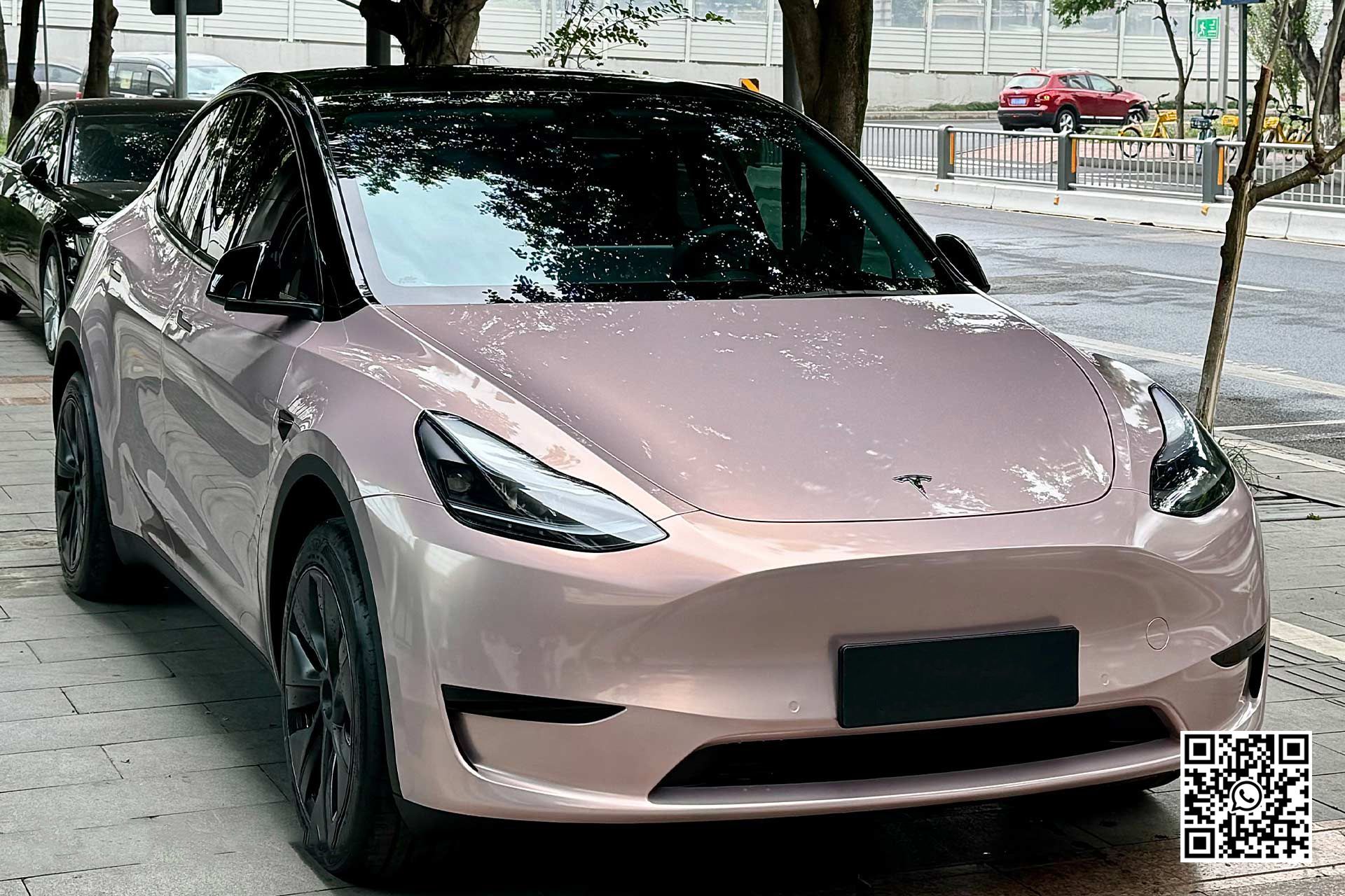 una tesla model y rosa è parcheggiata in una strada accanto a un albero .