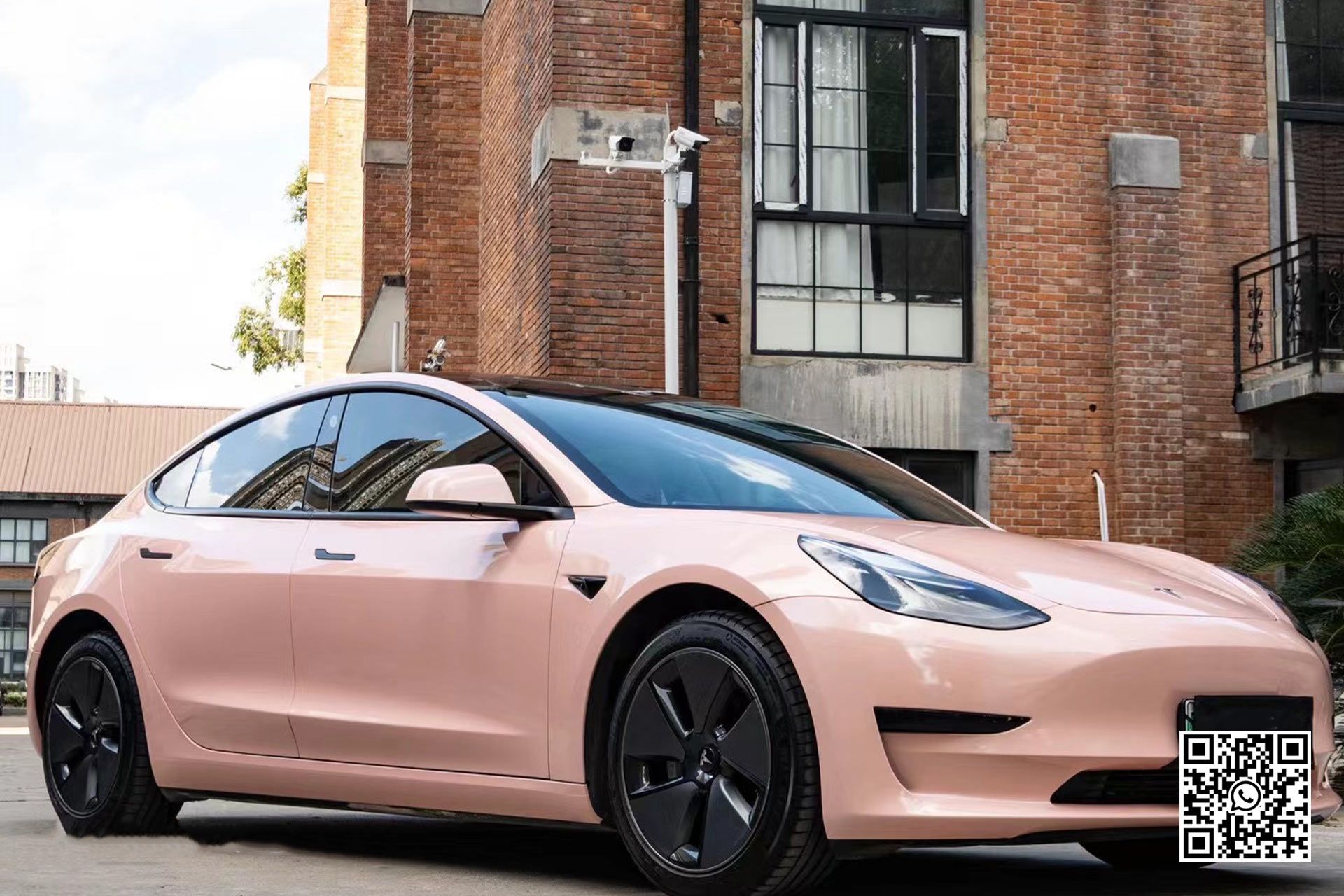 una tesla model 3 rosa è parcheggiata davanti a un edificio in mattoni .