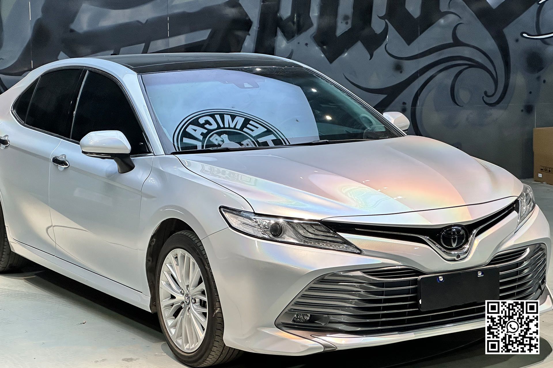 una toyota camry bianca è parcheggiata davanti a un muro di graffiti .