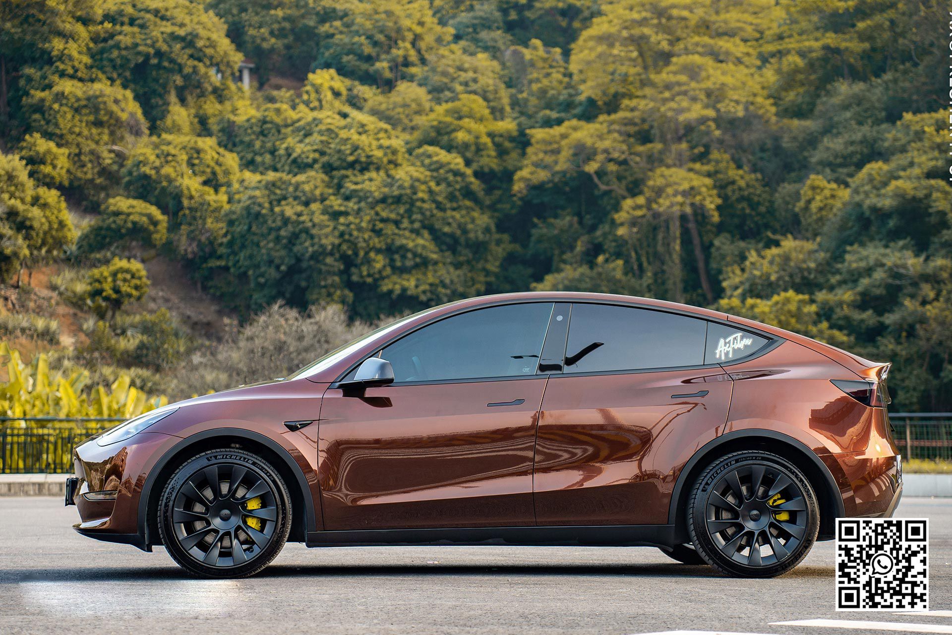 una tesla model y marrone è parcheggiata su una strada accanto a una foresta .