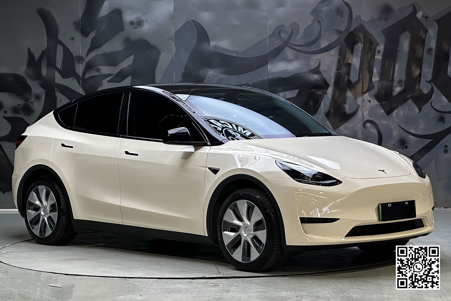 una tesla model y bianca è parcheggiata davanti a un muro di graffiti .