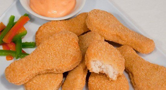 Un plato blanco cubierto con nuggets de pollo y verduras.