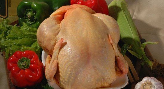 Un pollo entero está sobre una bandeja de poliestireno rodeado de verduras.