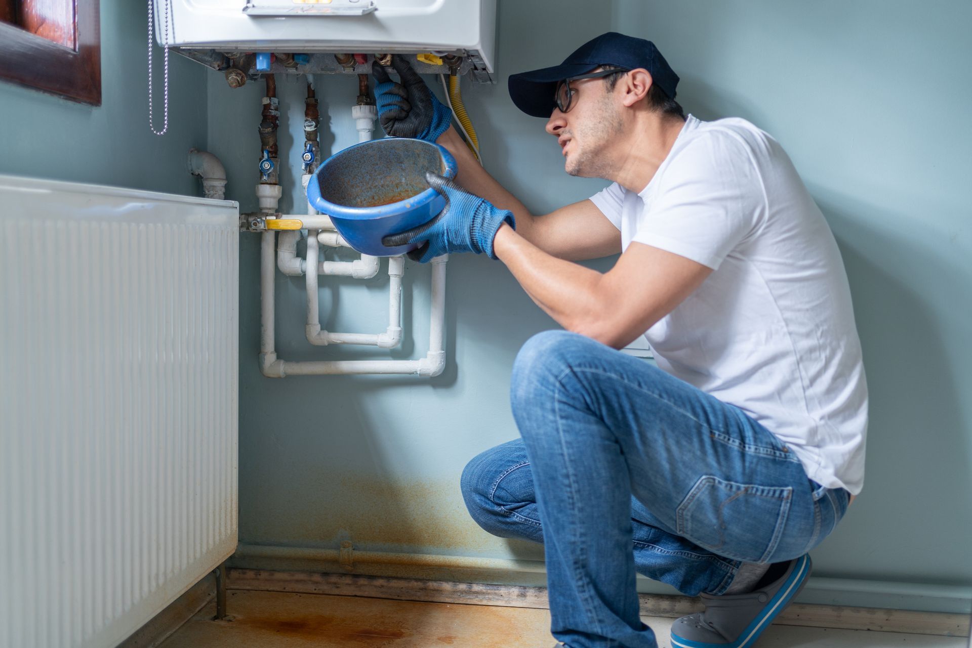 A man is kneeling down in a room fixing a boiler.