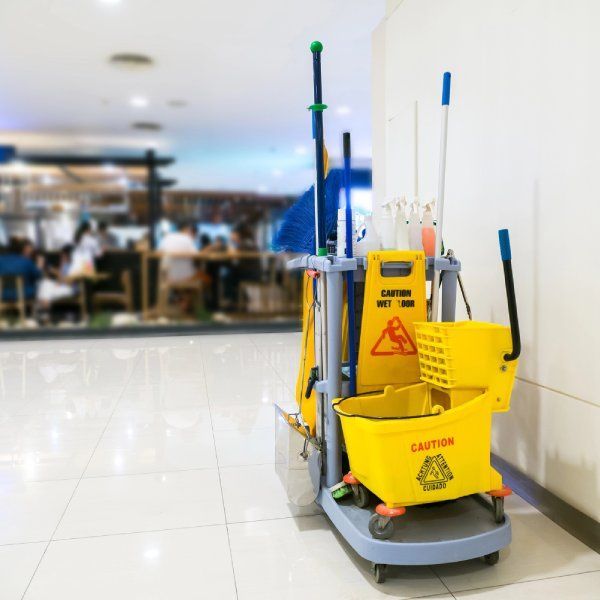 Janitorial cart with cleaning supplies near a workplace area.