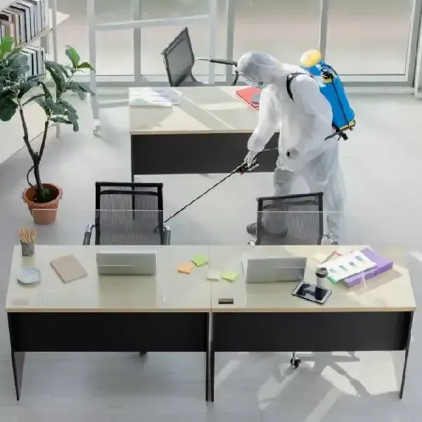 Worker in protective gear disinfecting office with spray equipment.