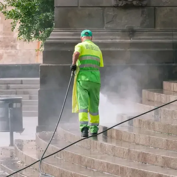 Worker power washing stone steps outside a commercial building.