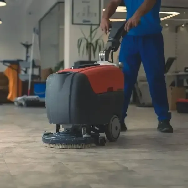 Janitor using floor scrubber machine on commercial flooring.