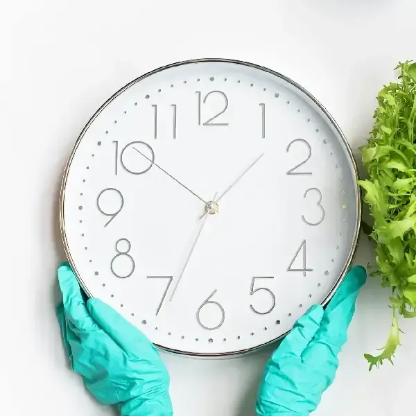 Gloved hands holding clock representing recurring cleaning schedule.