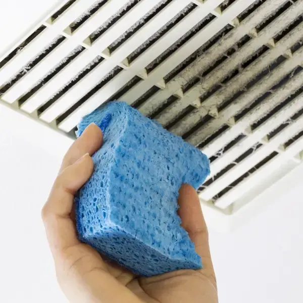 Hand cleaning dusty ceiling vent with blue sponge.