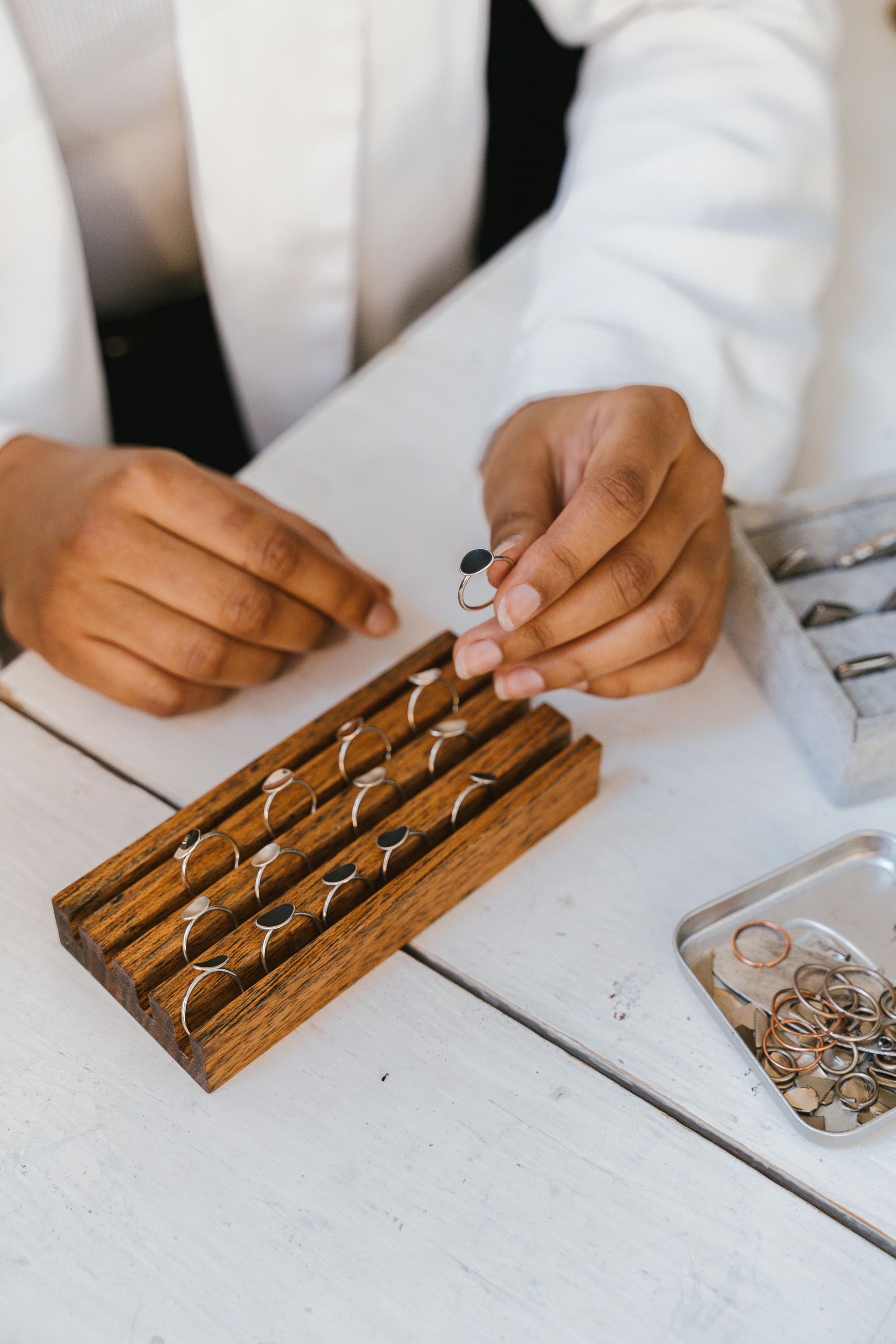 Person in white coat arranging rings on a wooden display and a white table.