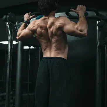 A shirtless man is doing pull ups on a bar in a gym.