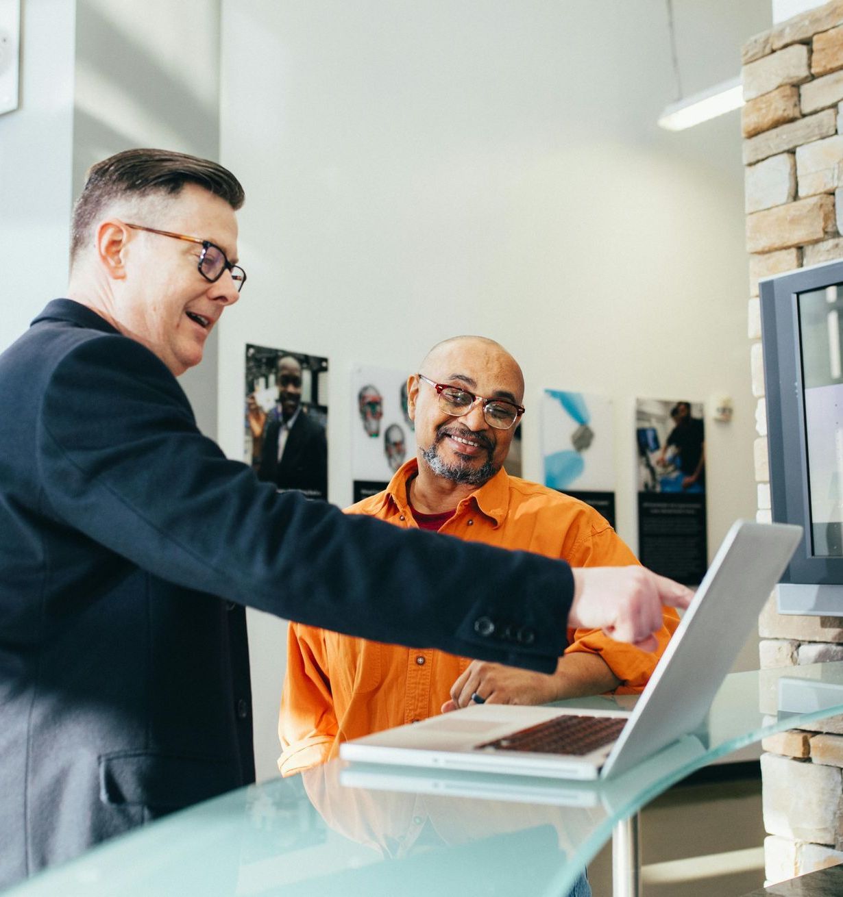 A man is pointing at a laptop while another man looks on