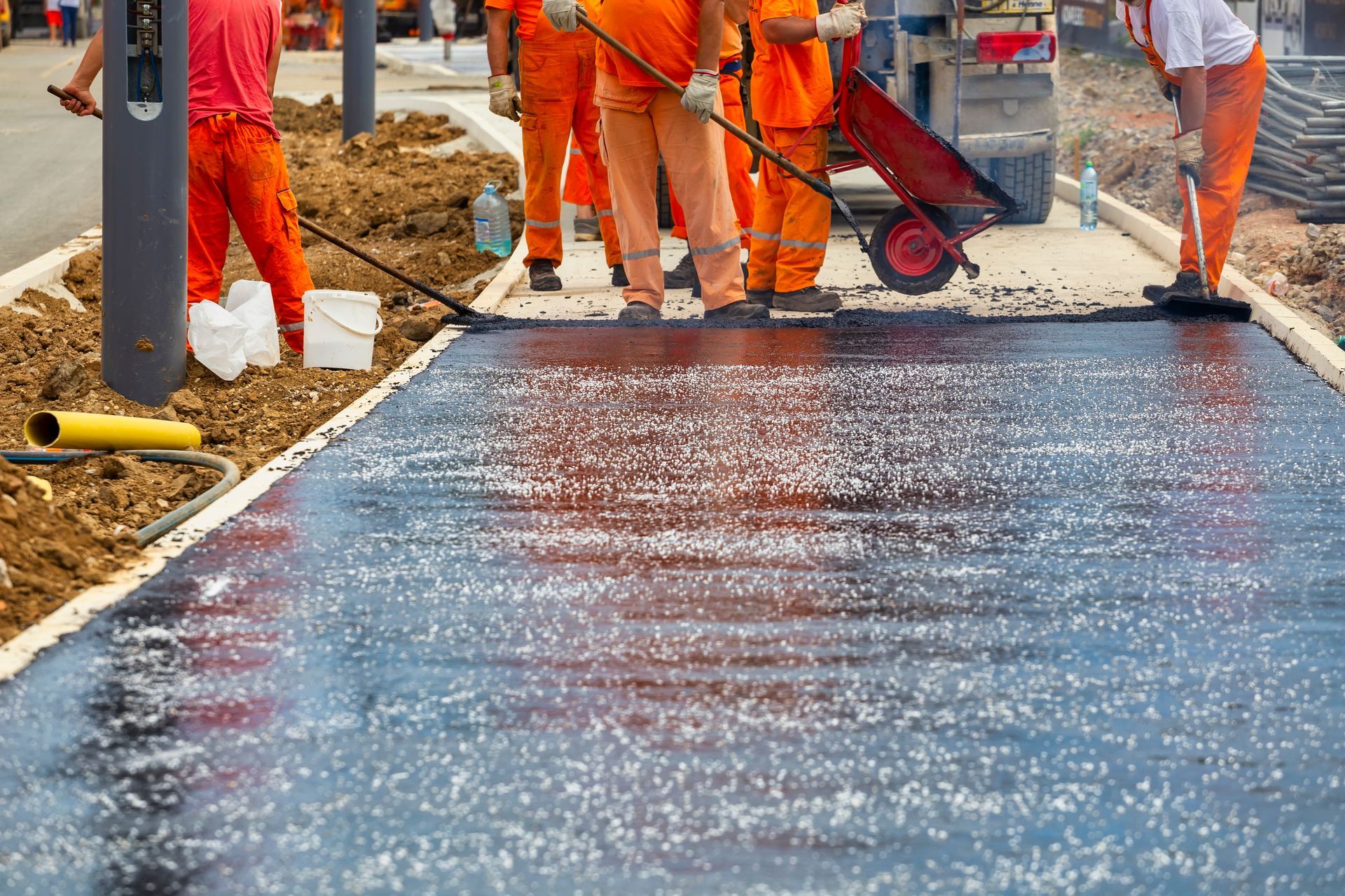 Construction crew applying fresh asphalt pavement using hand tools on a roadway.