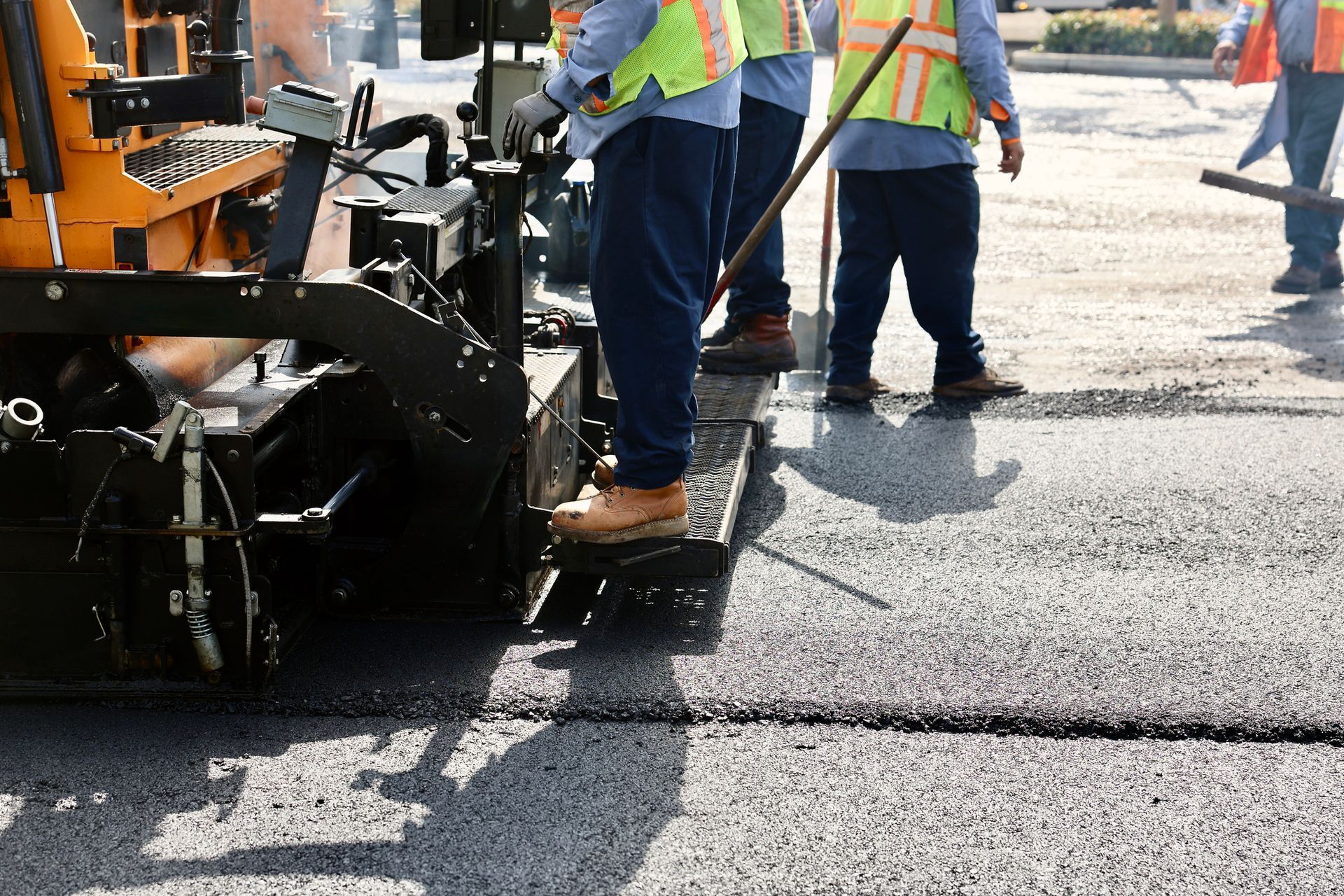 Asphalt repair contractors operate a machine, spreading hot asphalt on a road project.