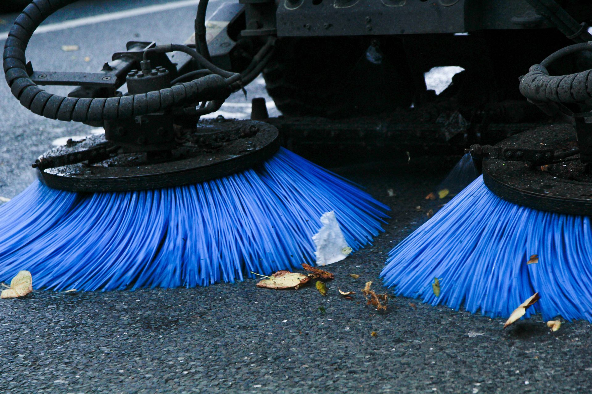 Street sweeper brushes cleaning road with scattered leaves and debris. Street sweeper brushes cleaning road with scattered leaves and debris.