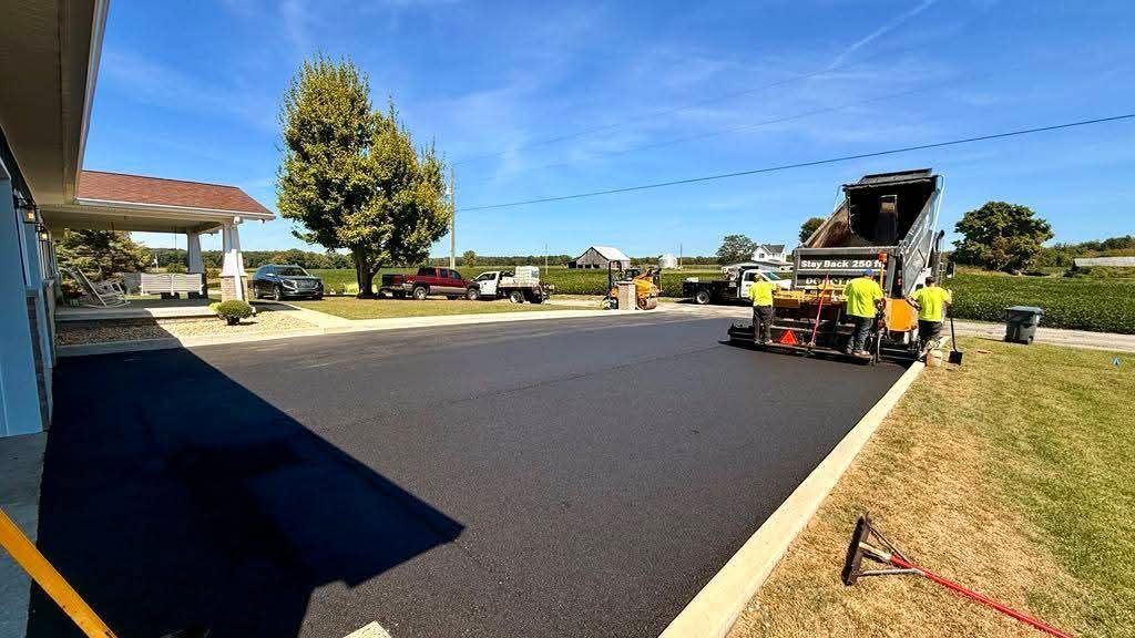 A contractor wearing jeans levels the concrete on the ground with a rake next to it.