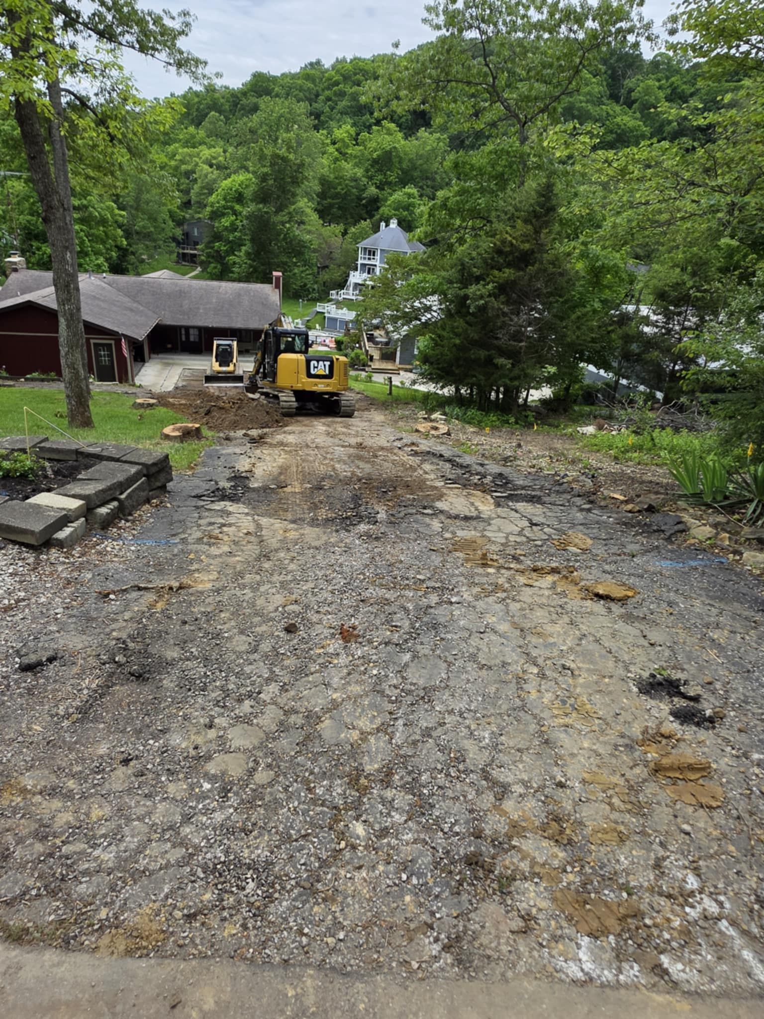 A bulldozer is driving down a dirt road next to a house.