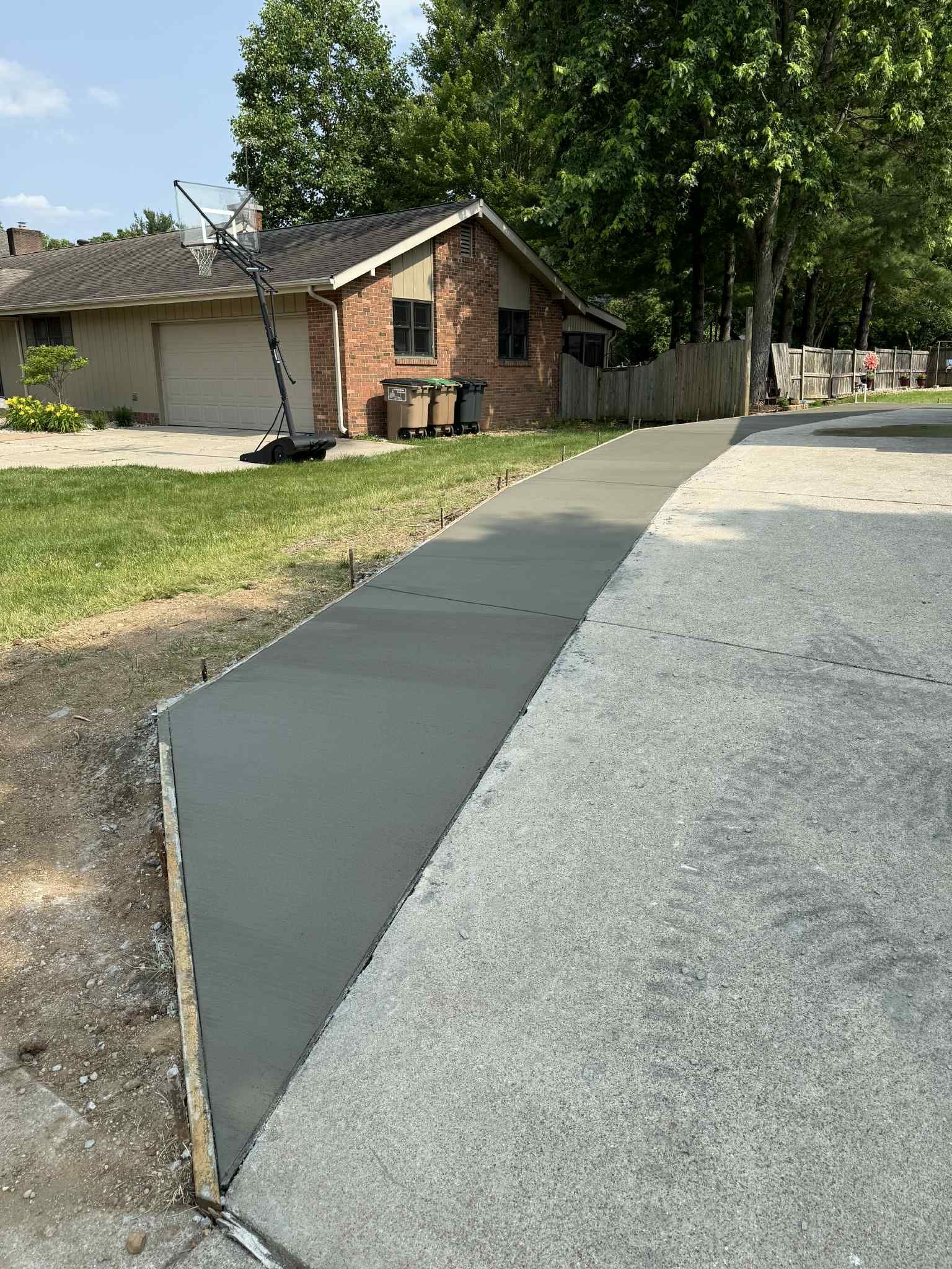 A concrete driveway is being built in front of a brick house.