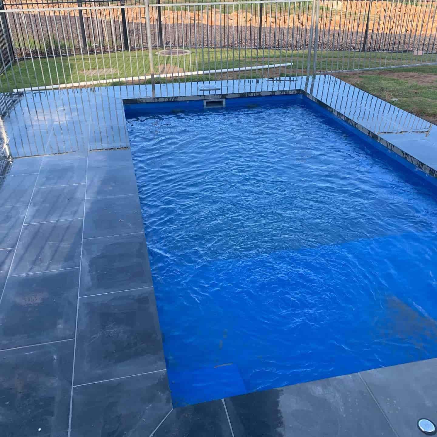 A Large Blue Swimming Pool with A Metal Fence Around It — Creative Spaces Landscaping in Dubbo, NSW